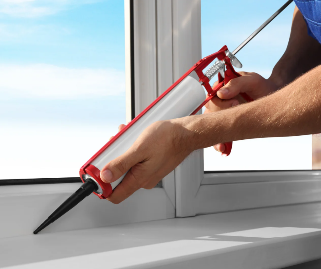 person using caulk gun to seal window