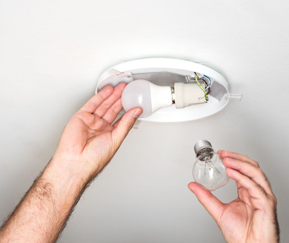 Person replacing a lightbulb in a light fixture in the ceiling